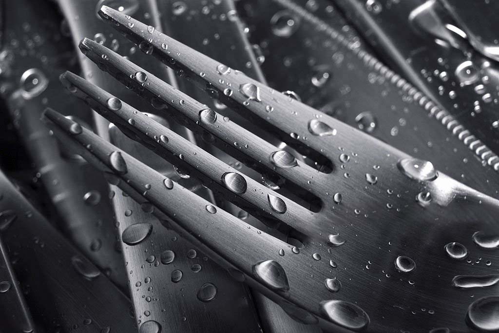 Water beading up and rolling off the surface of a black titanium spoon, showing its protective qualities