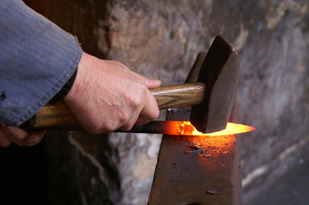 A glowing hot bar of steel being forged by a mechanical hammer