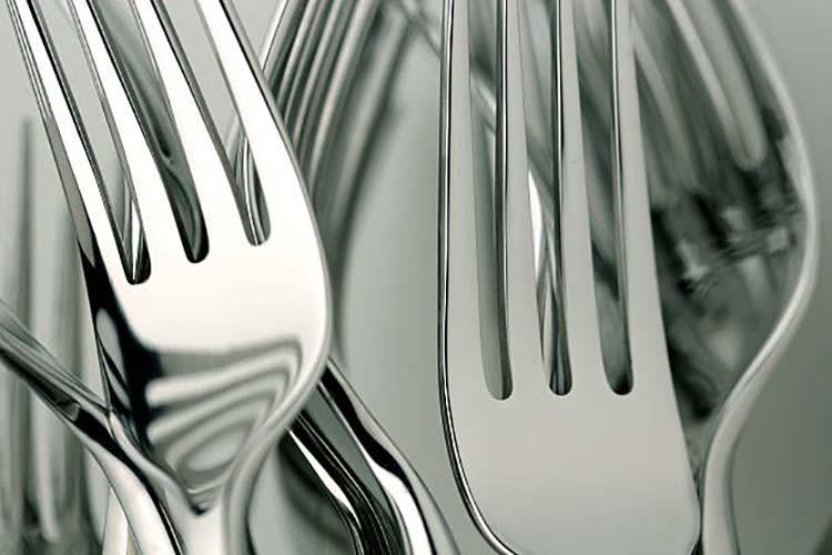 A hand weighing a fork and spoon, feeling the balance and quality