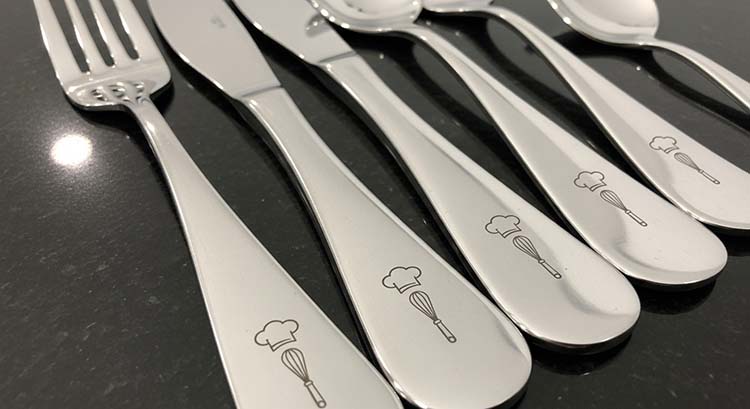 A close-up shot of a laser beam engraving a detailed logo onto a stainless steel knife