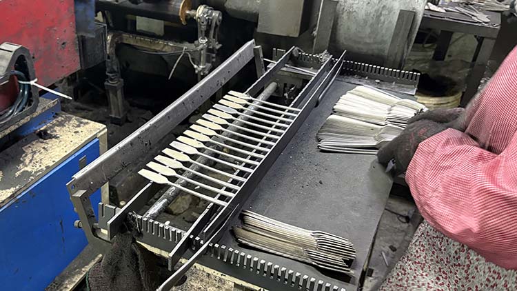 A factory line with a QC technician measuring a fork right after it comes out of a stamping machine