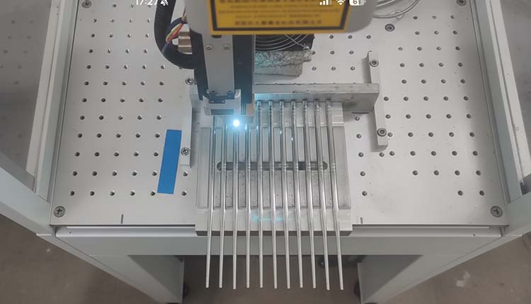 A custom jig holding multiple fork handles in precise alignment under a laser engraver