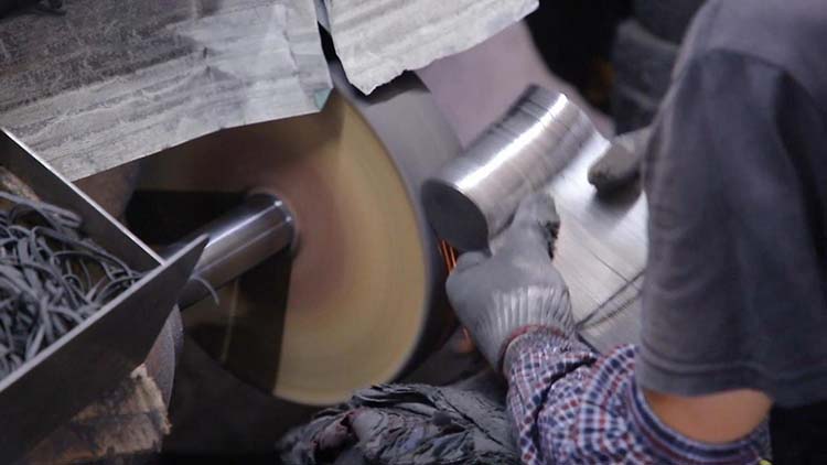 A skilled worker carefully hand-polishing the intricate handle of a fork on a buffing wheel