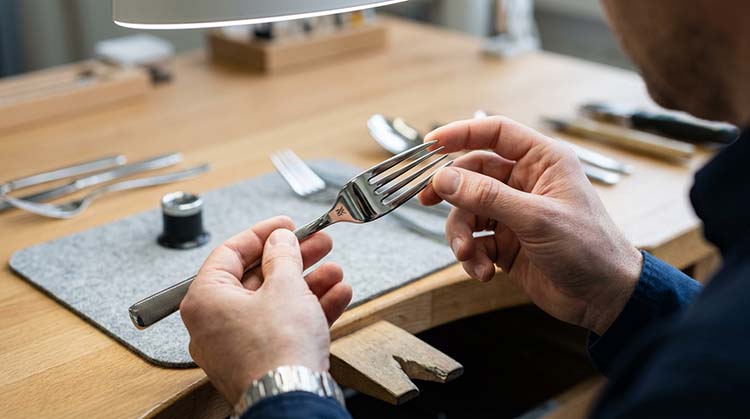 An inspector carefully running their finger along the edge of a fork