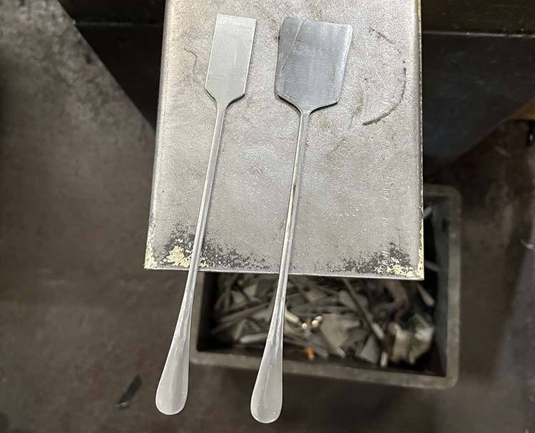 A machine rolling the handle of a stainless steel spoon blank to the correct thickness