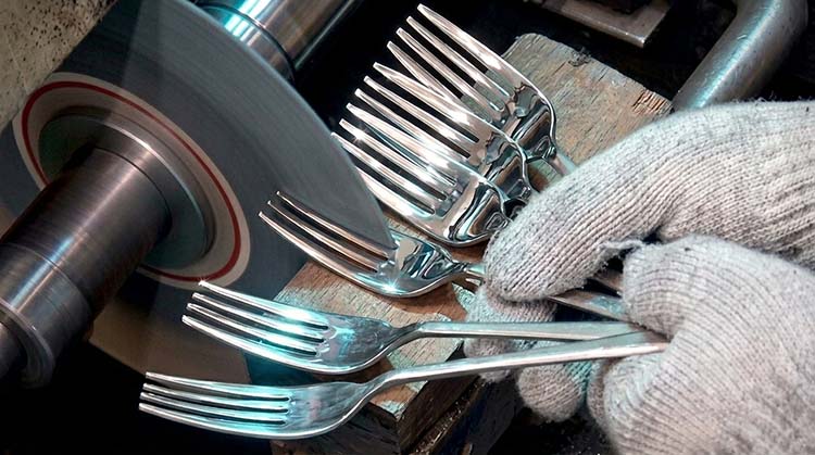 A factory worker meticulously polishing a spoon by hand