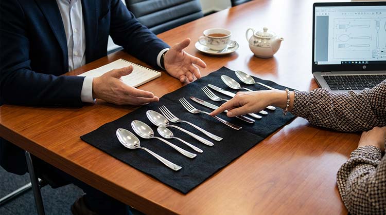 Two people, a client and a supplier, discussing flatware samples over a table